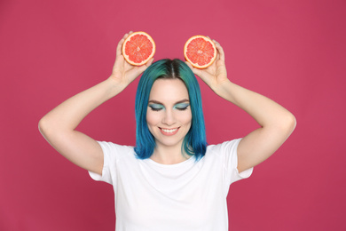 Photo of Young woman with bright dyed hair holding grapefruit on pink background