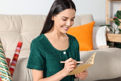 Photo of Happy woman writing message in greeting card on floor in living room