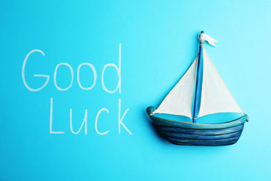 Photo of Phrase GOOD LUCK and boat on light blue background, top view