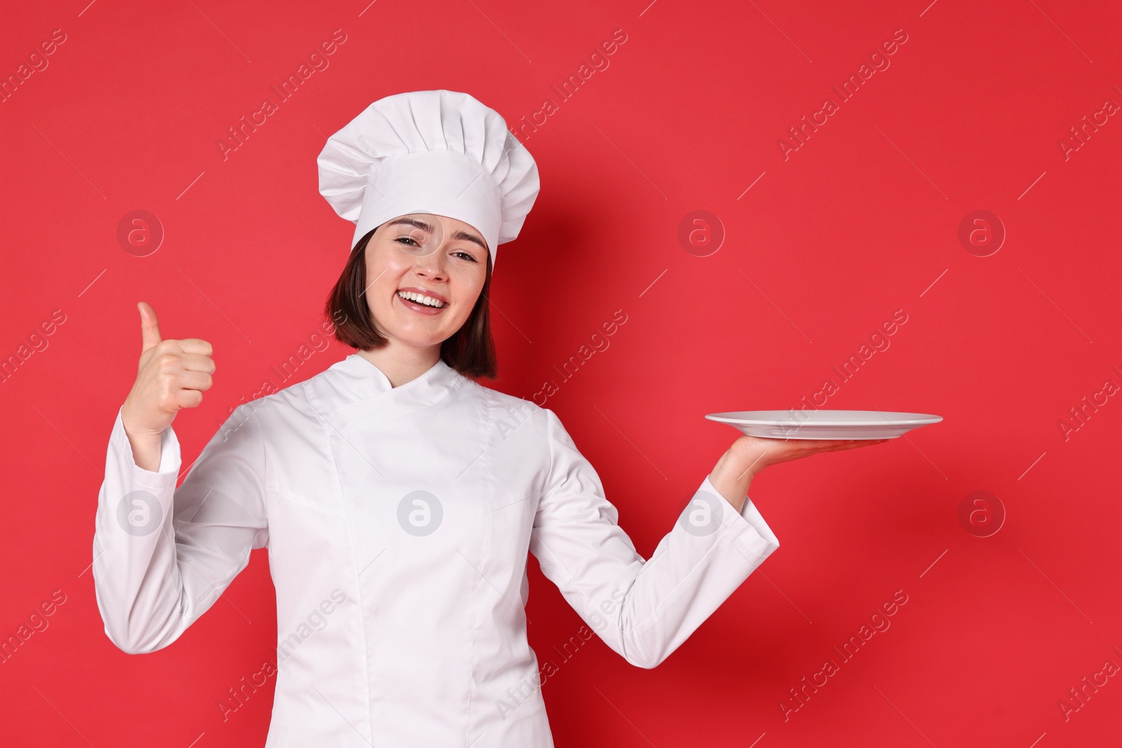 Photo of Happy confectioner with plate showing thumbs up on red background
