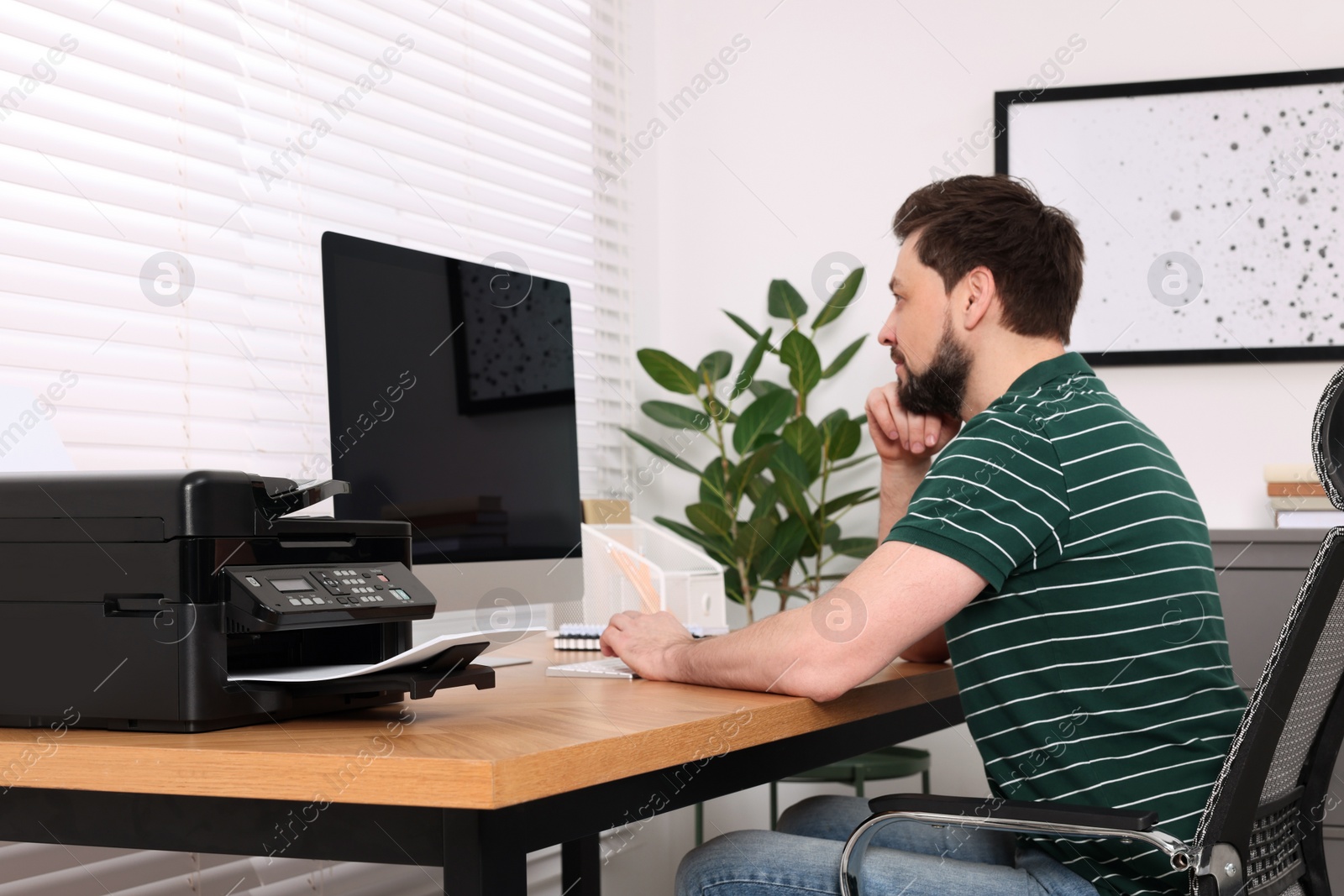 Photo of Man using modern printer at wooden table indoors