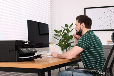Photo of Man using modern printer at wooden table indoors