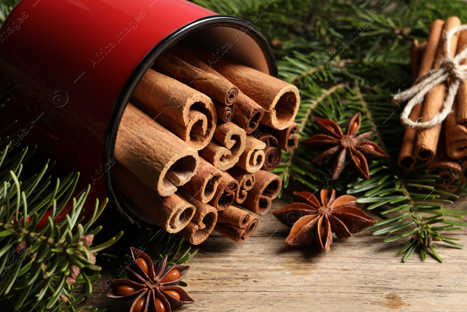 Photo of Many cinnamon sticks, anise stars and fir branches on wooden table, closeup