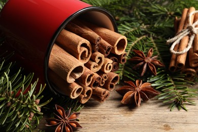 Photo of Many cinnamon sticks, anise stars and fir branches on wooden table, closeup
