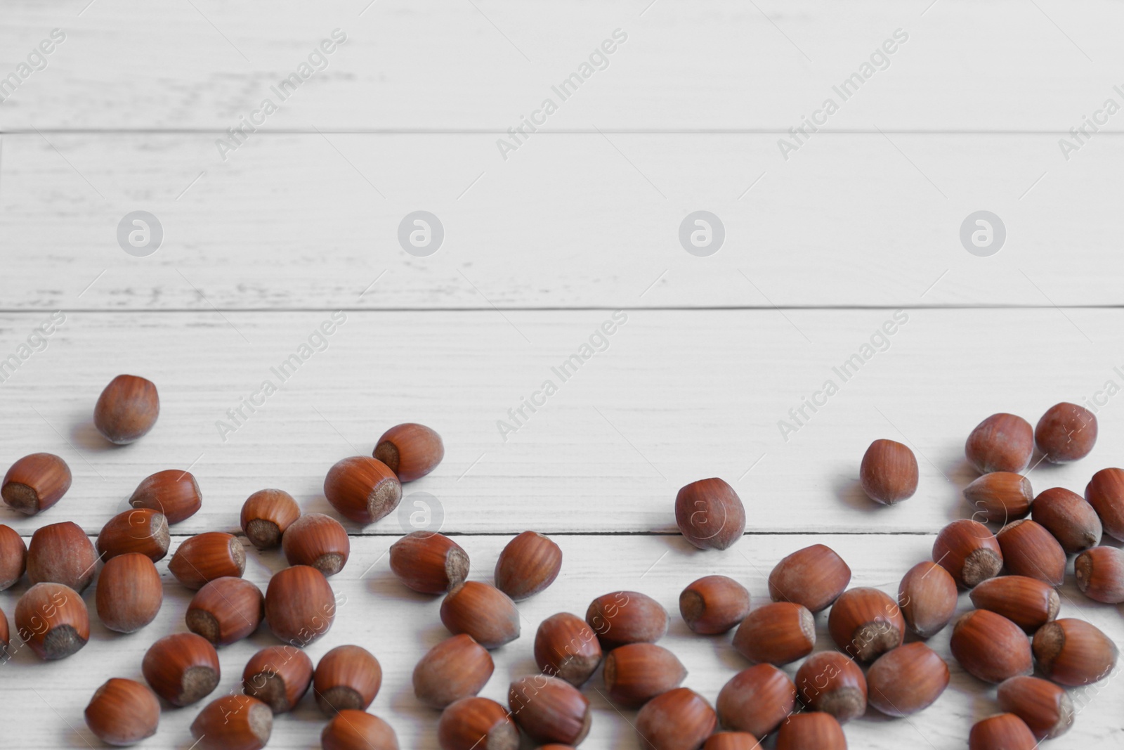 Photo of Tasty hazelnuts on white wooden table, flat lay. Space for text