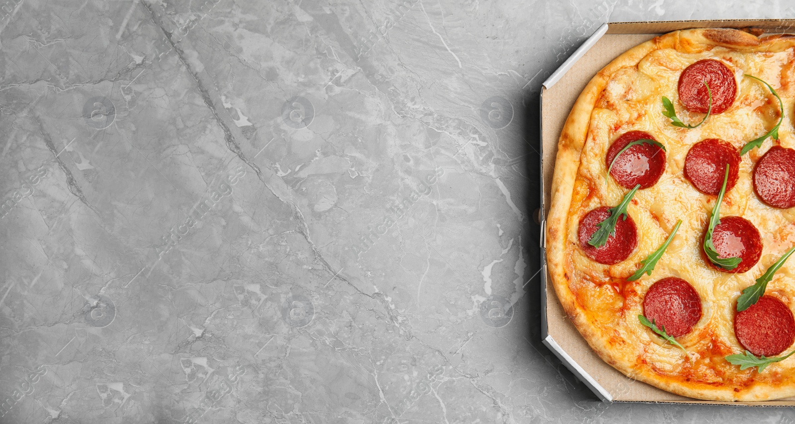 Photo of Tasty pepperoni pizza in cardboard box on light grey marble table, top view. Space for text