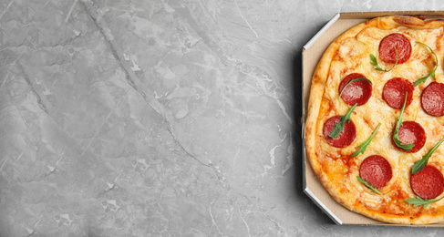 Photo of Tasty pepperoni pizza in cardboard box on light grey marble table, top view. Space for text