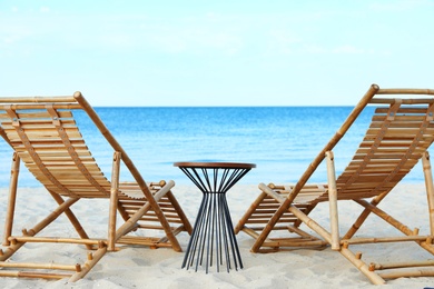 Photo of Empty wooden sunbeds and table on sandy shore. Beach accessories
