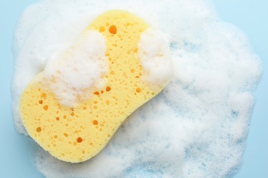 Photo of Yellow sponge with foam on light blue background, top view