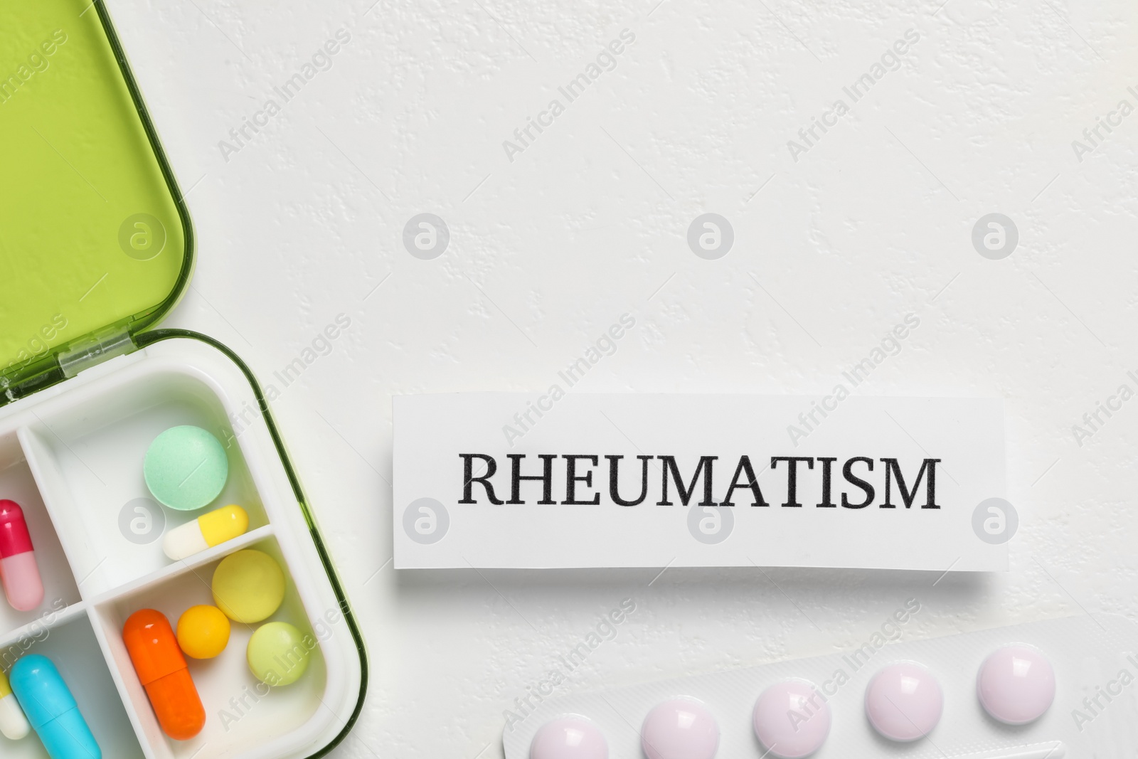 Photo of Card with word Rheumatism and pills on white background, flat lay. Space for text