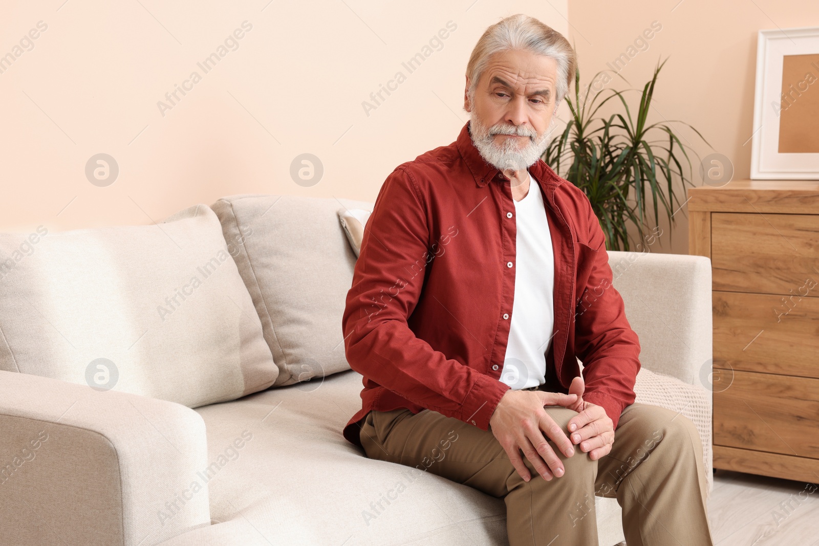 Photo of Senior man suffering from pain in his knee at home. Arthritis symptoms