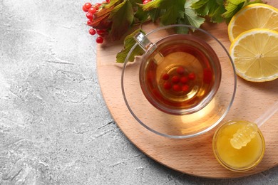 Cup of delicious tea with lemon, honey and viburnum on light grey table, flat lay. Space for text
