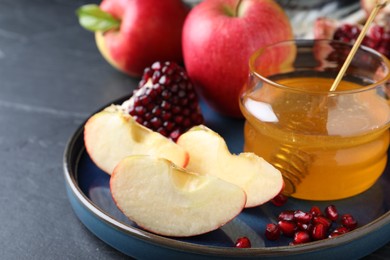 Photo of Honey, pomegranate and apples on black table, closeup. Rosh Hashana holiday