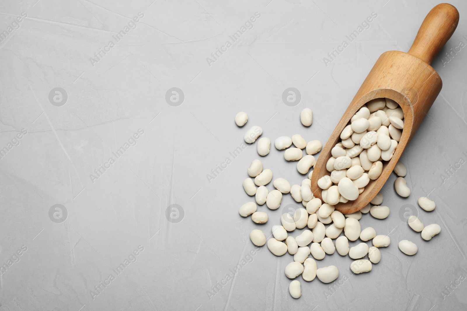 Photo of Wooden scoop with raw white beans on light grey table, flat lay. Space for text