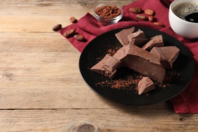 Photo of Pieces of tasty milk chocolate and cocoa powder on wooden table, space for text