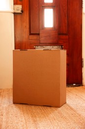 Photo of Delivery service. Cardboard on rug near wooden door indoors