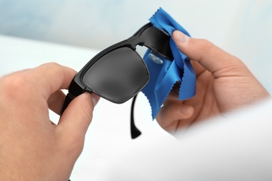 Man wiping sunglasses with microfiber cleaning cloth indoors, closeup