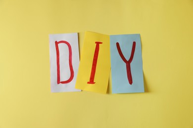 Photo of Abbreviation DIY made of papers with letters on yellow background, flat lay
