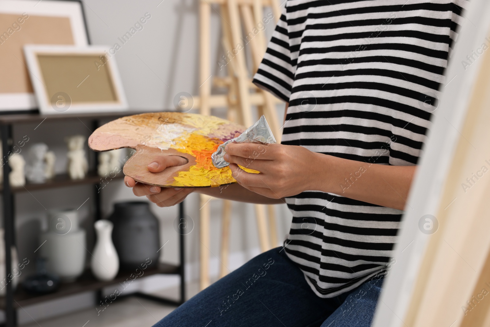 Photo of Young woman mixing paints on palette in studio, closeup