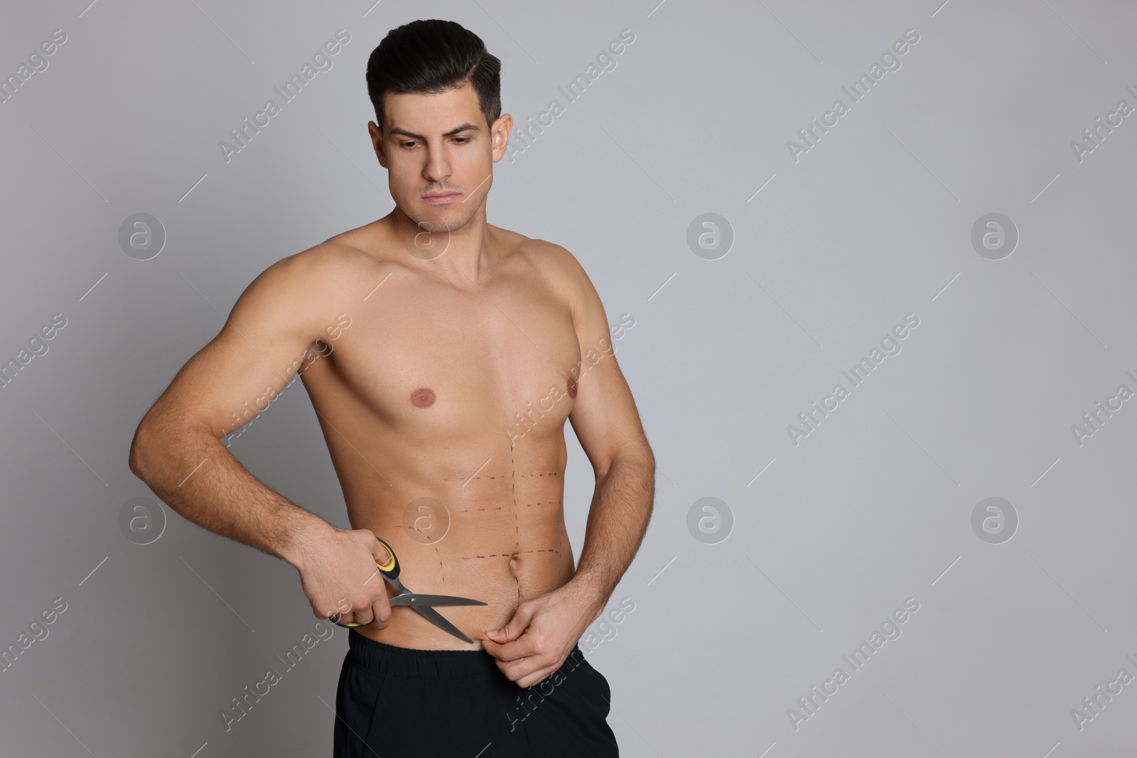 Photo of Fit man with scissors and marks on body against grey background, space for text. Weight loss surgery