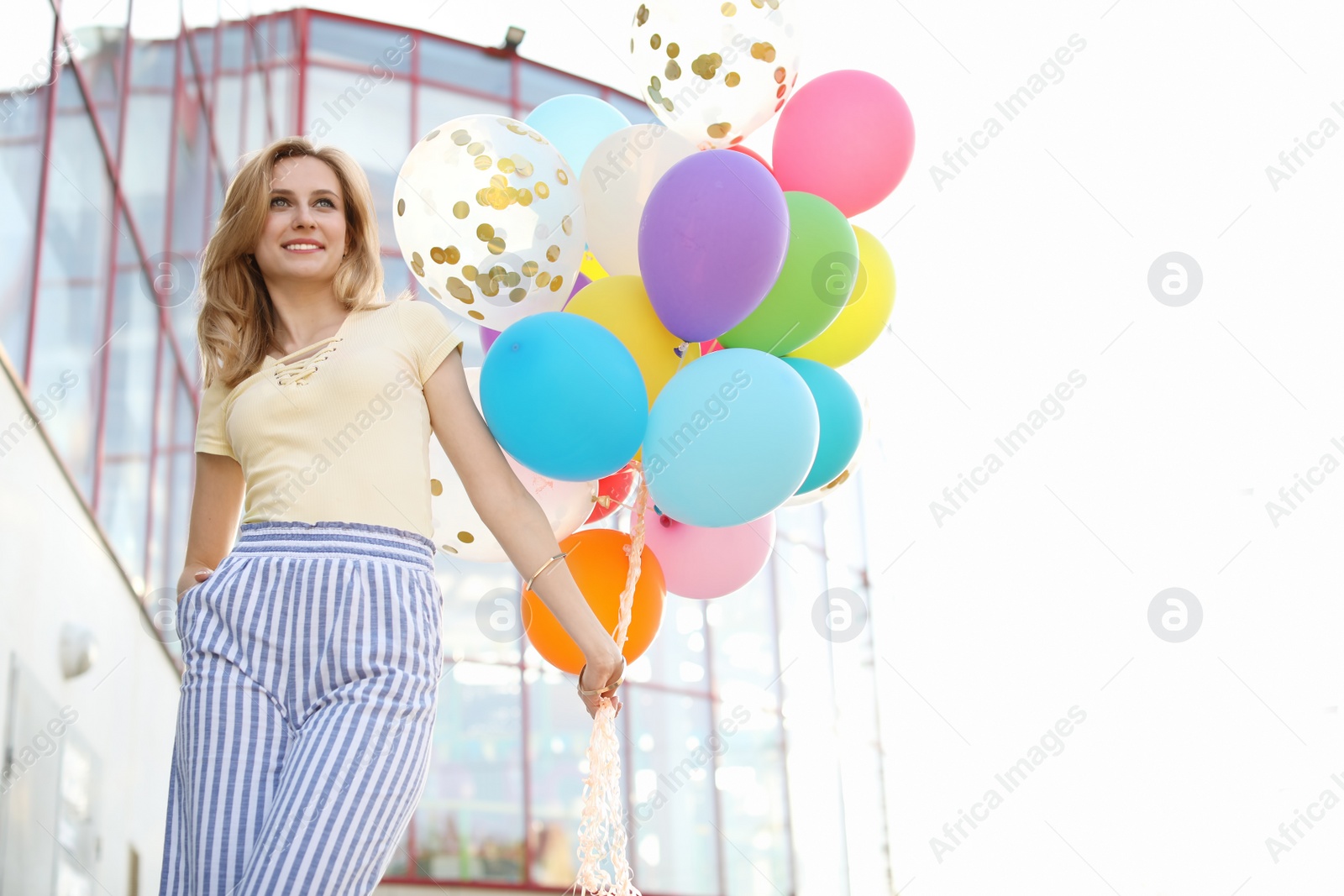 Photo of Young woman with colorful balloons outdoors on sunny day