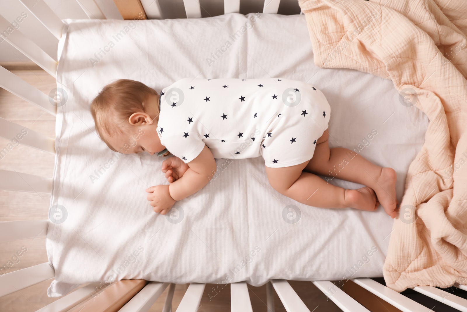 Photo of Adorable little baby with pacifier sleeping in crib indoors, top view