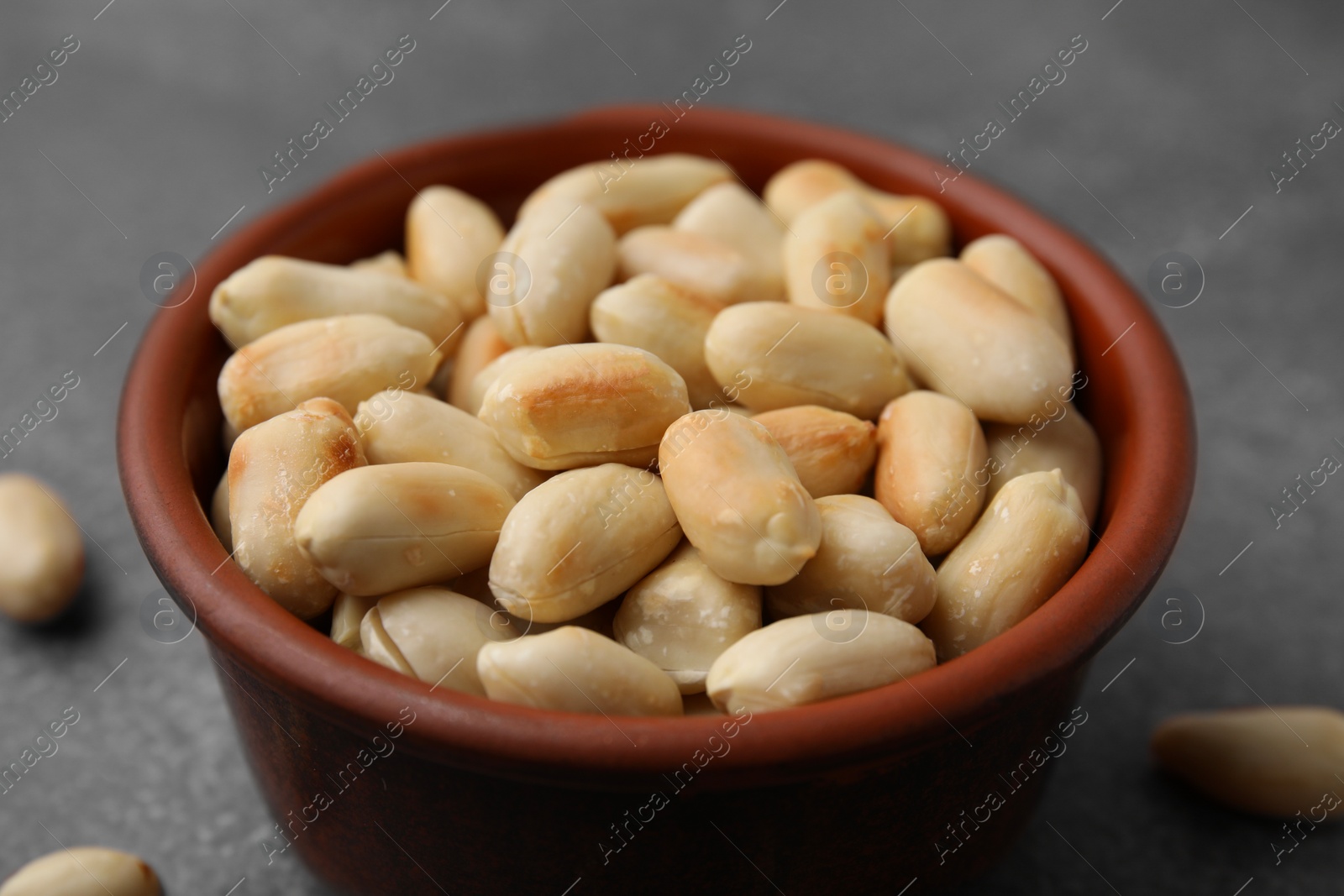 Photo of Roasted peanuts in bowl on brown table, closeup