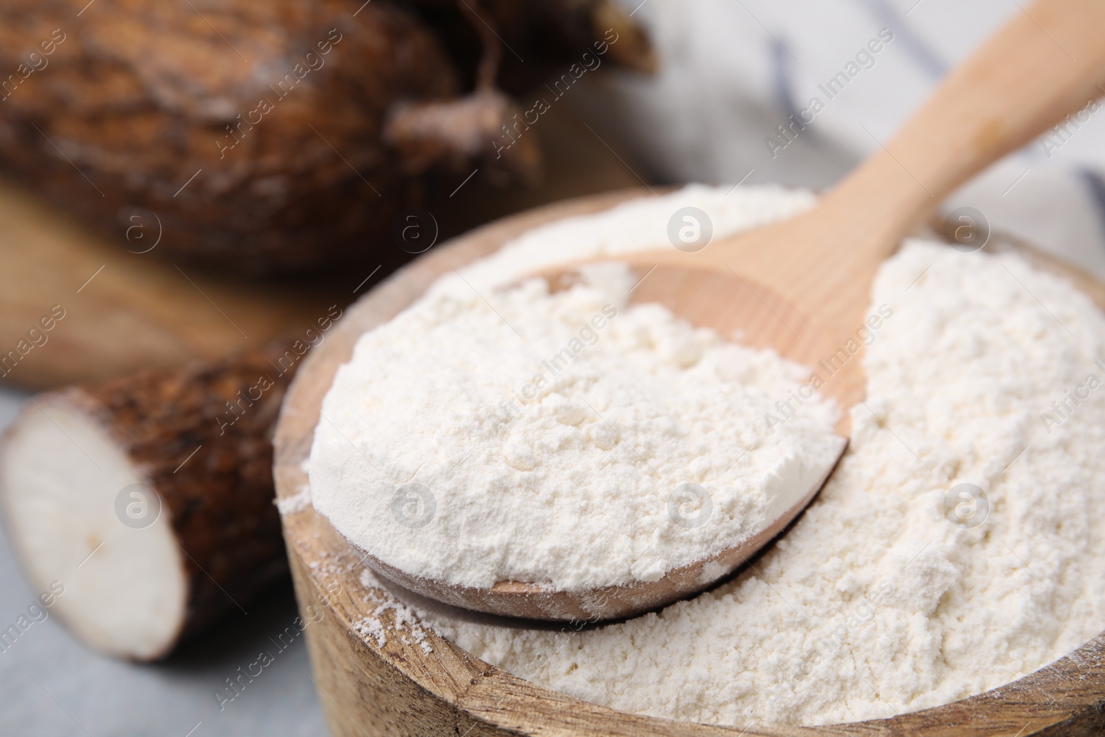 Photo of Wooden bowl and spoon with cassava flour on table, closeup