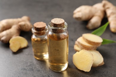 Glass bottles of essential oil and ginger root on grey table