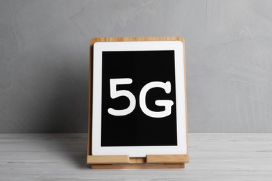 Internet concept. Tablet with 5G phrase and stand on white wooden table