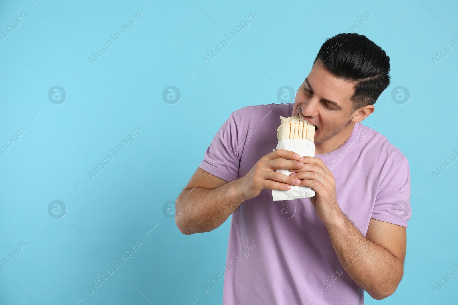 Photo of Man eating delicious shawarma on turquoise background, space for text