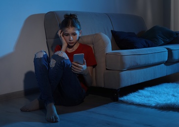 Photo of Emotional teenage girl with smartphone in dark room. Danger of internet