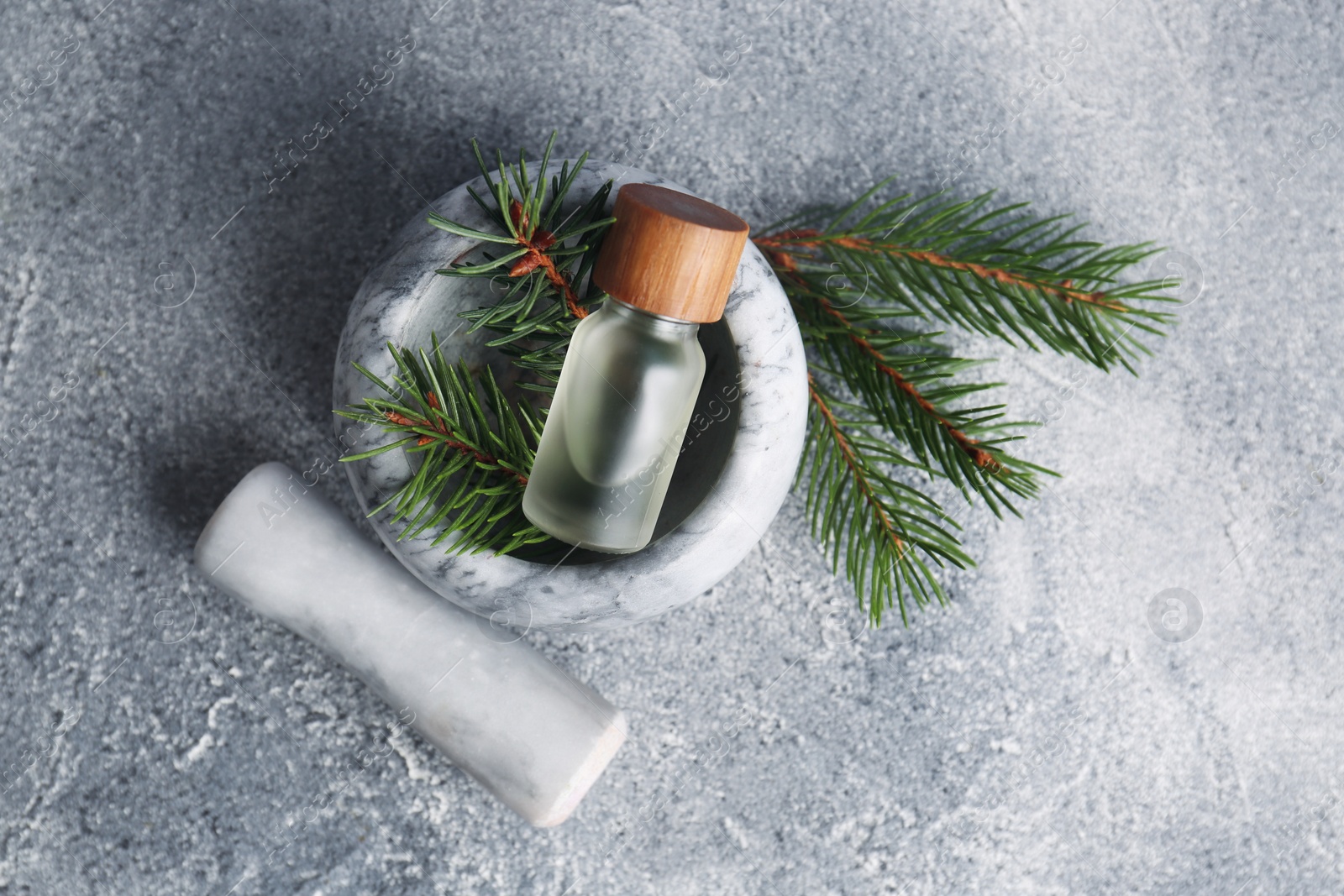 Photo of Bottle of aromatic essential oil and mortar with pine branch on light grey table, flat lay