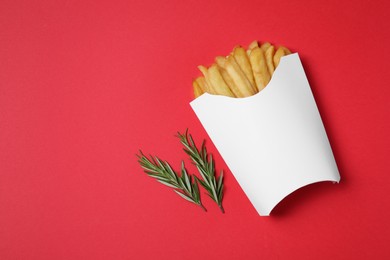 Paper cup with French fries and rosemary on red table, flat lay. Space for text