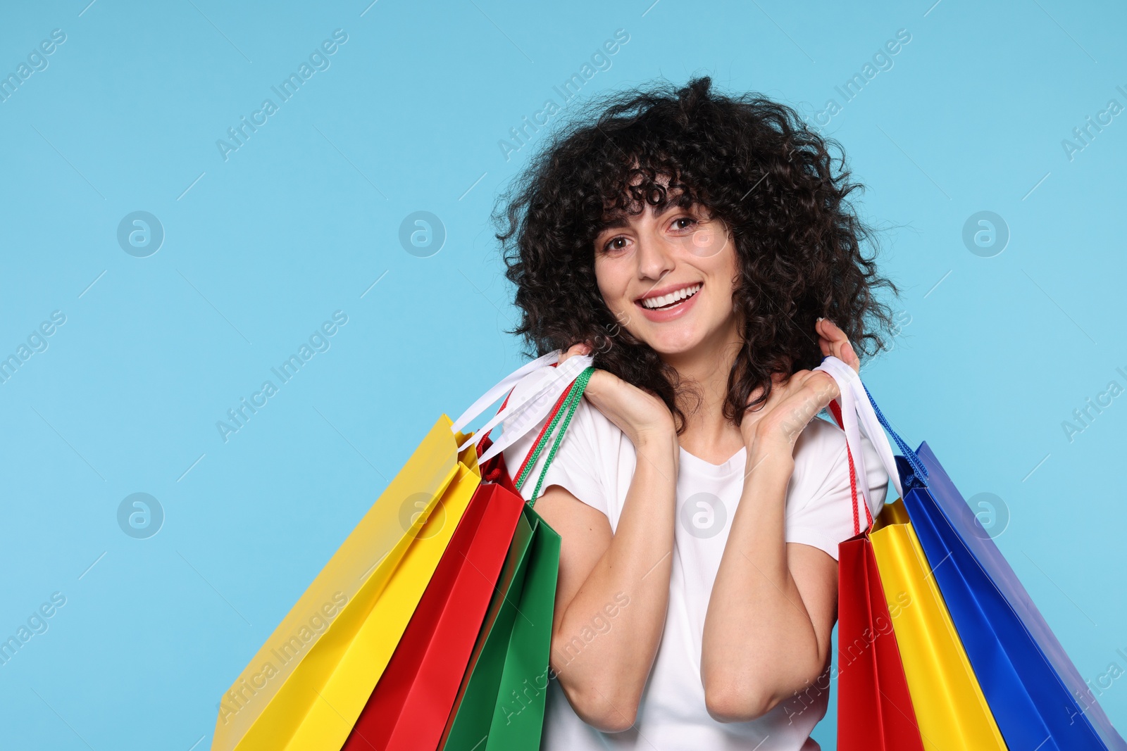 Photo of Happy young woman with shopping bags on light blue background