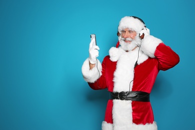 Santa Claus listening to Christmas music on color background