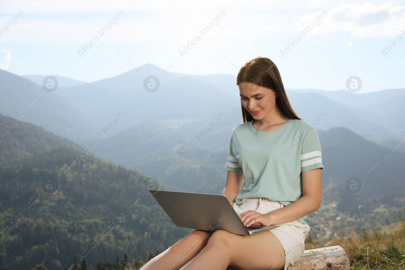 Photo of Young woman working with laptop in mountains on sunny day