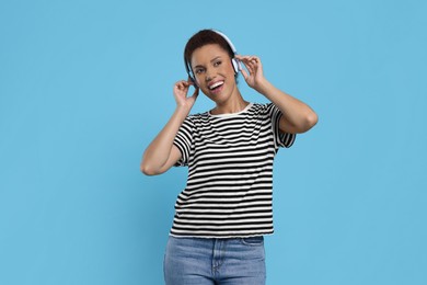 Happy young woman in headphones dancing on light blue background