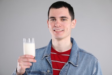 Happy man with milk mustache holding glass of tasty dairy drink on gray background