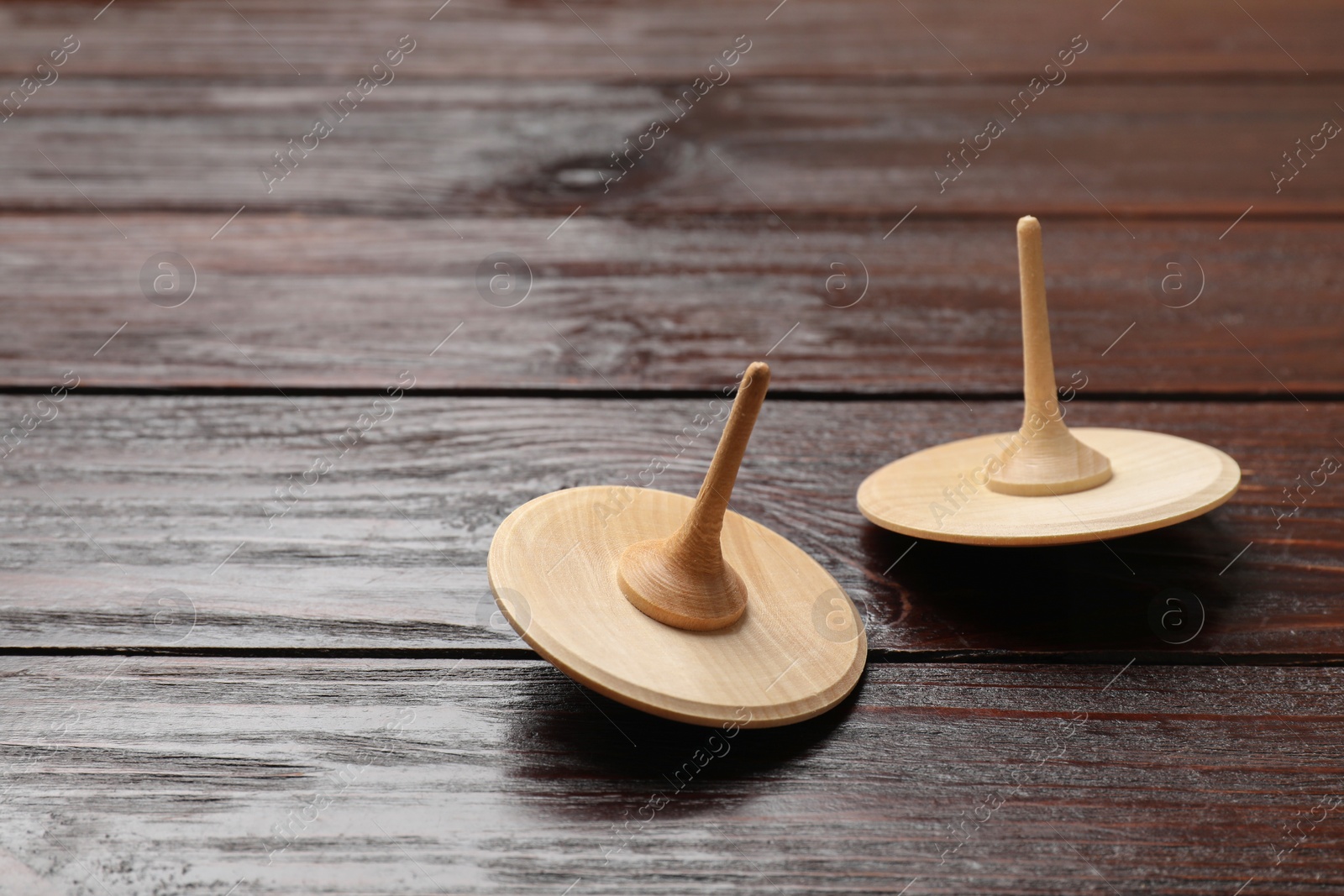 Photo of Two spinning tops on wooden table, closeup. Space for text