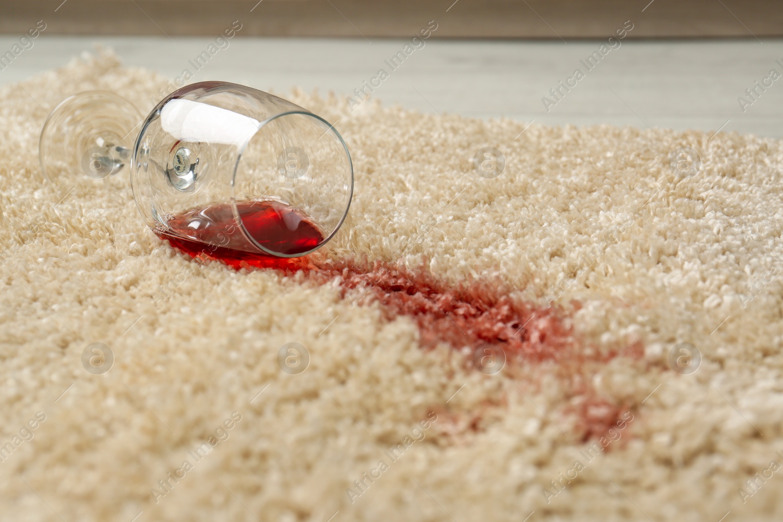 Photo of Overturned glass and spilled red wine on soft carpet, closeup