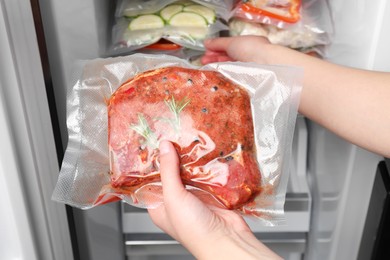 Photo of Woman putting vacuum bag with meat into fridge, closeup. Food storage