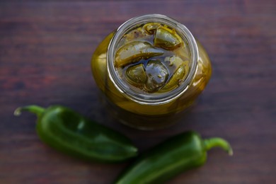 Photo of Fresh and pickled green jalapeno peppers on wooden table, top view