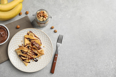 Delicious thin pancakes with chocolate spread, banana and nuts on light table, flat lay. Space for text