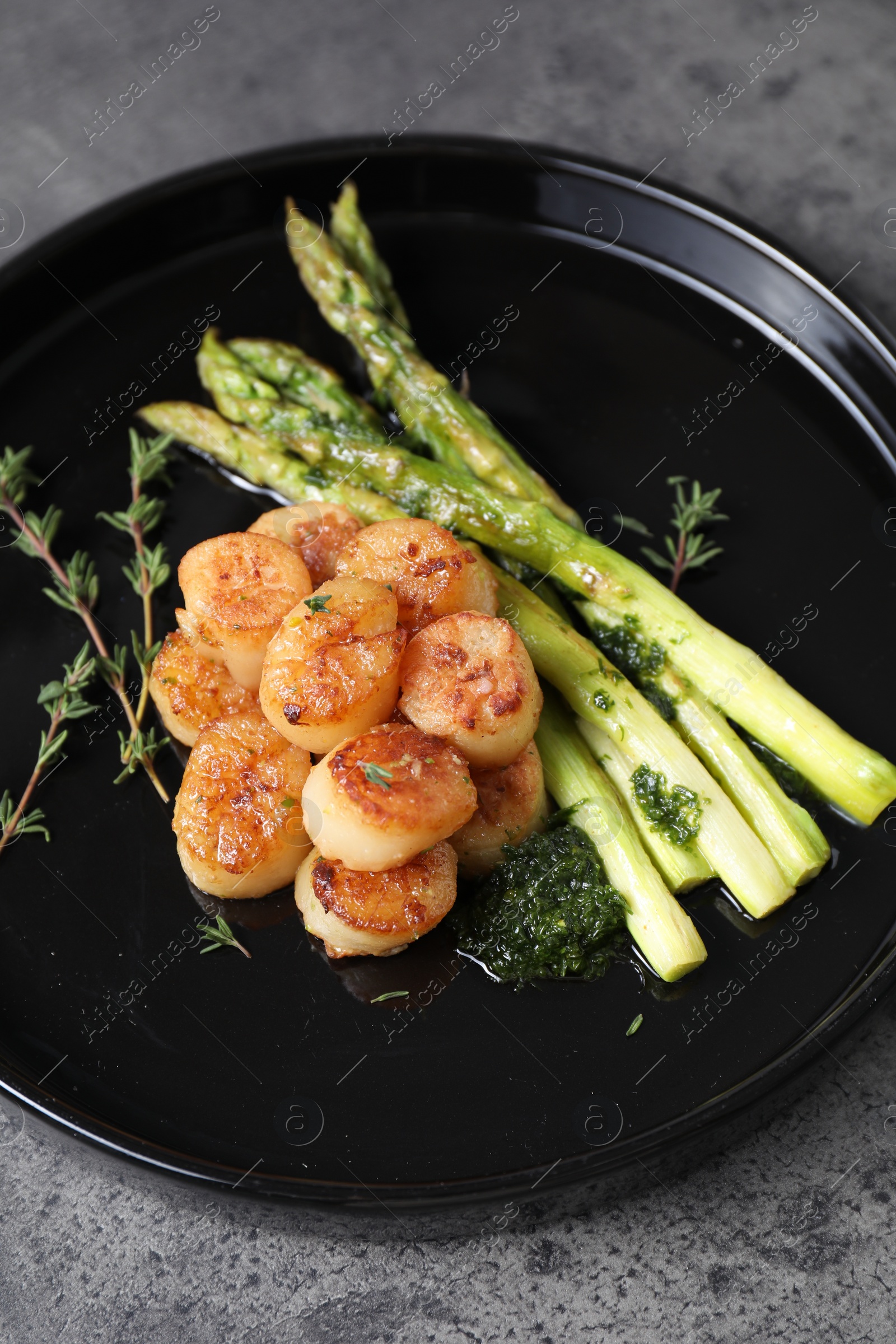 Photo of Delicious fried scallops with asparagus and thyme on grey table