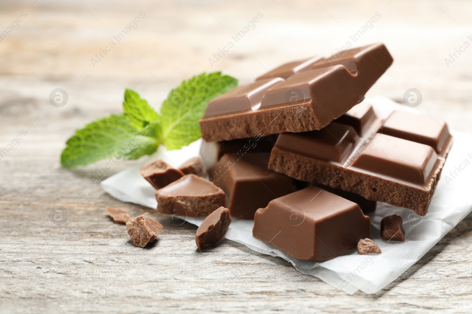 Photo of Pieces of milk chocolate with mint on wooden table