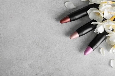 Photo of Set of bright lipsticks and spring flowers on grey background, flat lay. Space for text