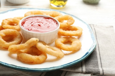 Plate with fried onion rings and sauce on table