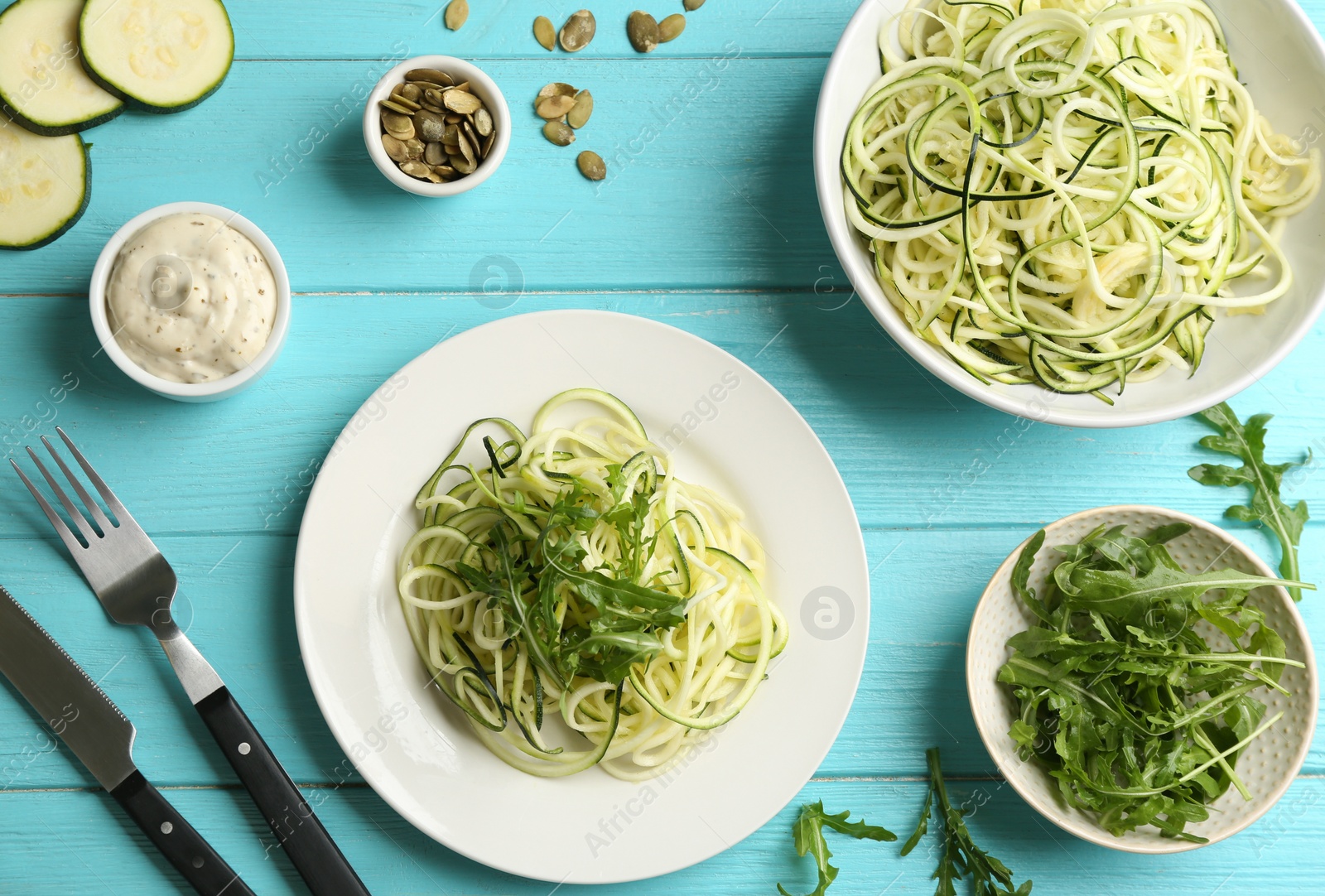 Photo of Delicious zucchini pasta with arugula served on light blue wooden table, flat lay