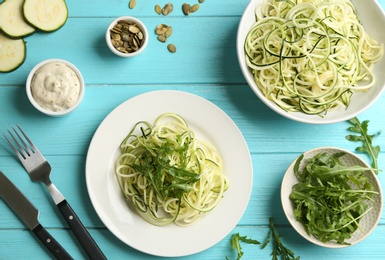 Photo of Delicious zucchini pasta with arugula served on light blue wooden table, flat lay